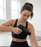 Jeune femme en tenue de sport utilisant le pistolet de massage Airona pour un auto-massage de l'épaule et du bras.